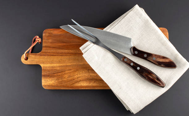 istock Wooden cutting board and fork and knife carving set on black background 1395952577