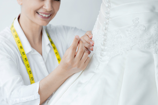 Unrecognizable female fashion designer at work. She is working on a wedding dress.