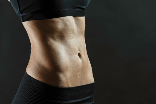 Belly of an unrecognizable slim caucasian woman wearing black sportswear  in front of black background. Representing being healthy and slim after regular workout and healthy lifestyle.
Note : Image is not body shape retouched.