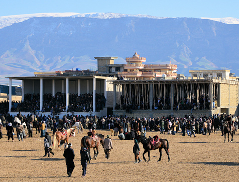 Mazar-e-Sharif, Balkh province, Afghanistan: seated and mounted spectators at a match of Buzkash aka Afghan polo, Afghanistan's national sport - horse-mounted players fight for a calf carcass - unfenced grounds, admission is open and free - mountains in the background.
