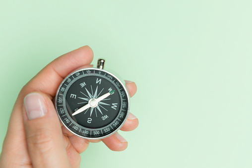 Hand is holding a compass in hand over green background.