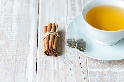 Herbal tea with cinnamon sticks on white wooden background.