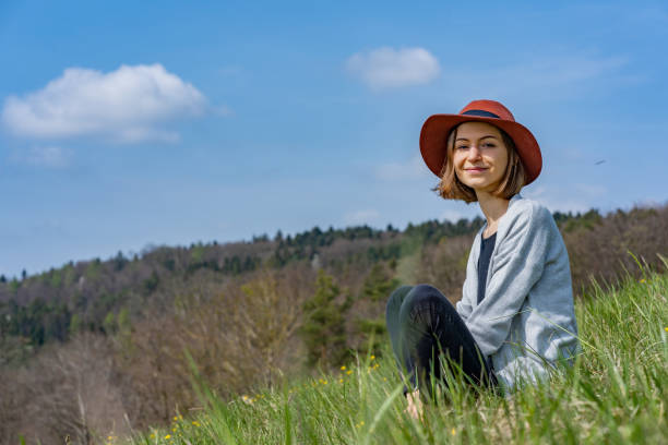 Portrait of young beautiful woman with hat, sitting in yellow spring flowers in Switzerland and looking away. stock photo