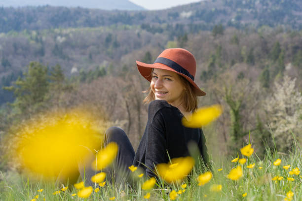 Portrait of young beautiful woman with hat, sitting in spring flowers. stock photo