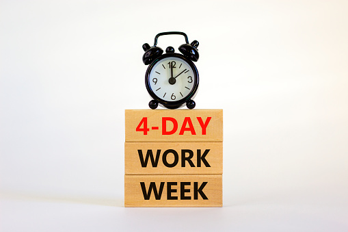 4-day work week symbol. Concept words '4-day work week' on wooden blocks. Black alarm clock. Beautiful white background. Copy space. Business and 4-day work week concept.