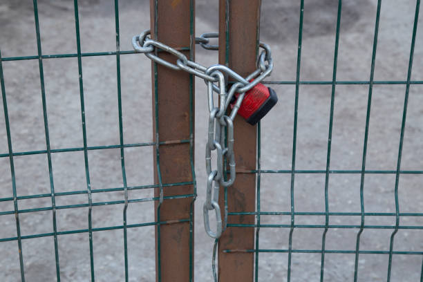 Red metal padlocks attached to a fence with buildings beyond.