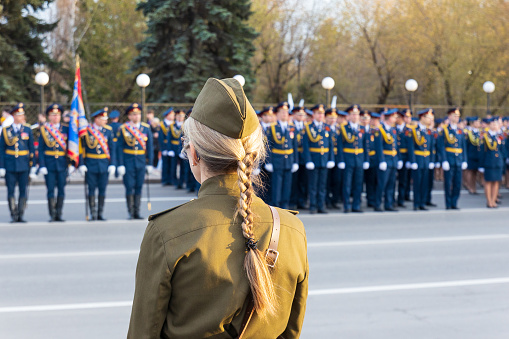 View from behind the back of a woman in a military Soviet uniform on the blurry ranks of military men in dress uniform. Rehearsal of the Victory Military Parade in the Great Patriotic War.