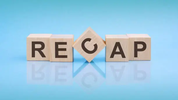 RECAP - word is written on wooden cubes close-up. blue background. white surface table