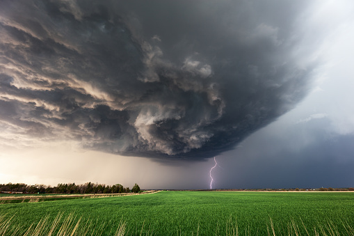 Dramatic supercell storm clouds with a lightning strike over a field in Kansas.