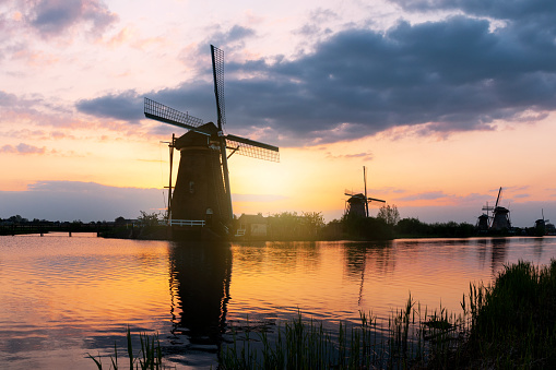 A collection of 18th Century traditional Dutch windmills reflected in water at sunset at Kinderdijk in South Holland.