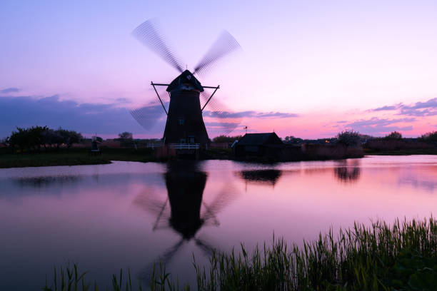 A 18th Century traditional Dutch windmills reflected in water at sunset at Kinderdijk in South Holland.