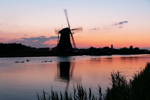 A 18th Century traditional Dutch windmills reflected in water at sunset at Kinderdijk in South Holland.