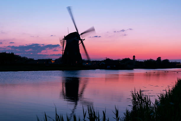 A 18th Century traditional Dutch windmills reflected in water at sunset at Kinderdijk in South Holland.