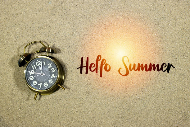 istock alarm showing twelve o'clock on sand with hello summer concept 1395969346
