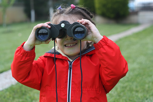 Four years old girl close up, looking through binoculars.