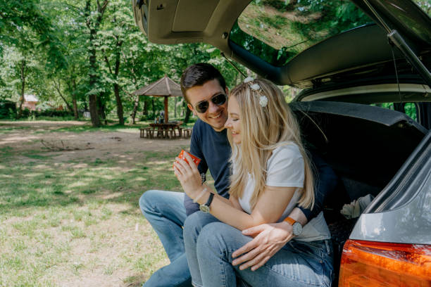 istock Happy young couple sitting in open car back, having stop off, drinking coffee. 1395970669