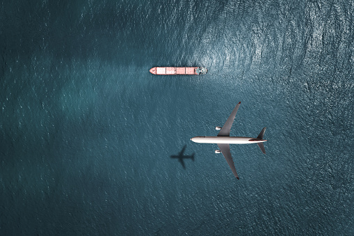 Airplane flying above cargo ship.