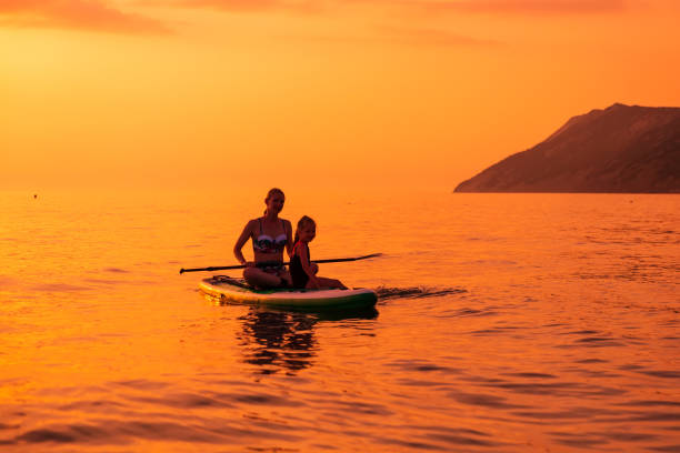 21. juni 2021. antalya, türkei. frau mit kindern paddelt abends auf stand up paddle board auf ruhiger see. frau und mädchen auf red paddle sup board mit farben des sonnenuntergangs - editorial women paddleboard surfboard stock-fotos und bilder