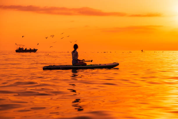 21. juni 2021. antalya, türkei. frau entspannt sich auf stand up paddle board bei ruhiger see mit sonnenuntergang oder sonnenaufgang. frau auf red paddle sup board und hellem sonnenuntergang mit reflexion - editorial women paddleboard surfboard stock-fotos und bilder