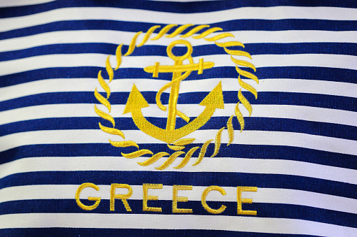 Sea anchor and text Greece on a background with a blue-white stripe