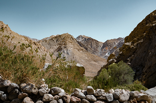 Horizontal shot of snow-capped mountain valley with vegetation and rock wall below, Chile