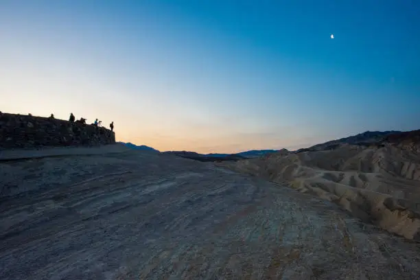 Photo of Zabriskie Point at Dawn with Moon and Silhouetted Photographers