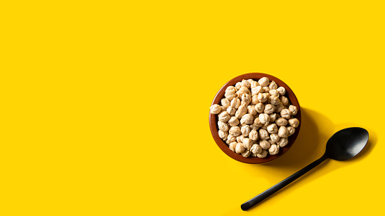 Chickpea beans on ceramic bowl  and black spoon on yellow modern background.