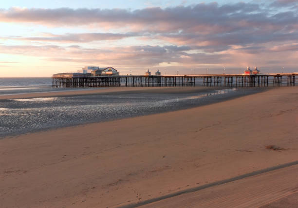 the sun setting over the historic north pier in blackpool with glowing light reflected on the beach and colourful twilight sky