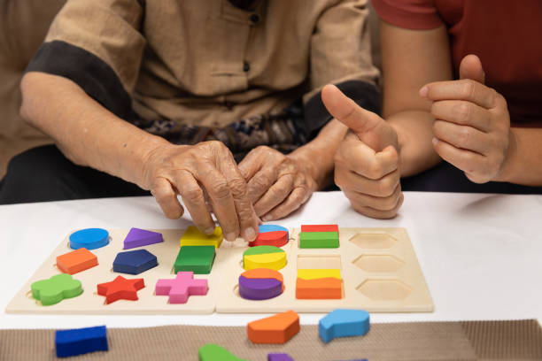 cuidadora y mujer mayor jugando rompecabezas de forma de madera para la prevención de la demencia - memorial fotografías e imágenes de stock