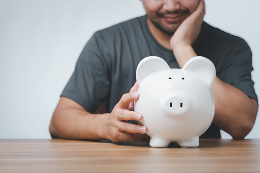 Asian men are thinking about what to do with their savings. Bearded man Happily sitting looking at the piggy bank