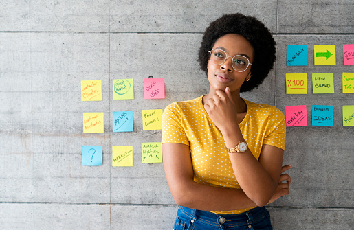Creative African American woman thinking about a business plan and using post-its on the wall