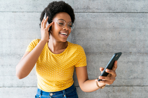 Portrait of a happy African American woman listening to music with headphones using her cell phone and smiling - lifestyle concepts