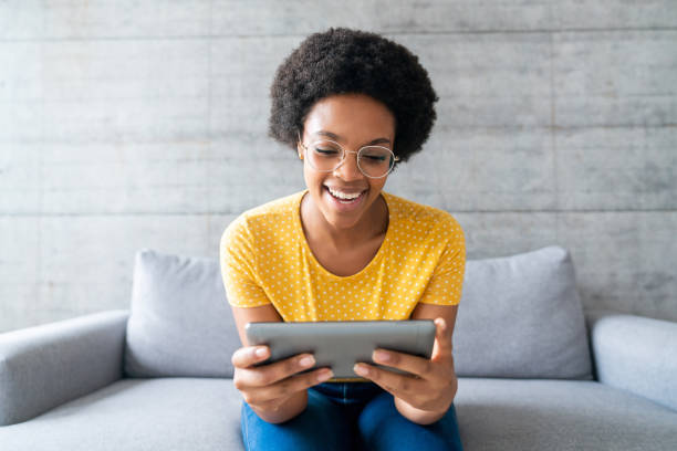 donna felice a casa che guarda video online su un tablet - watching foto e immagini stock