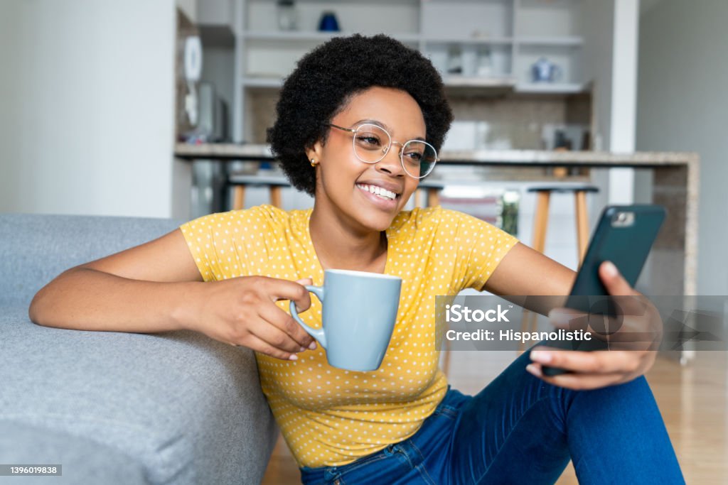 Woman looking at social media on her cell phone while taking a coffee break African American woman looking at social media on her cell phone while taking a coffee break Coffee Cup Stock Photo