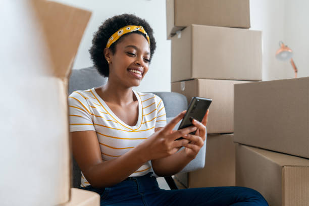 Happy woman checking her cell phone while moving house stock photo
