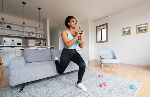 Beautiful African American woman exercising at home using dumbbells and smiling - healthy lifestyle concepts