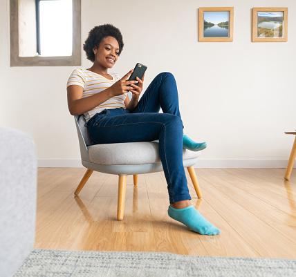 Happy African American woman relaxing at home and texting on her cell phone while smiling - lifestyle concepts