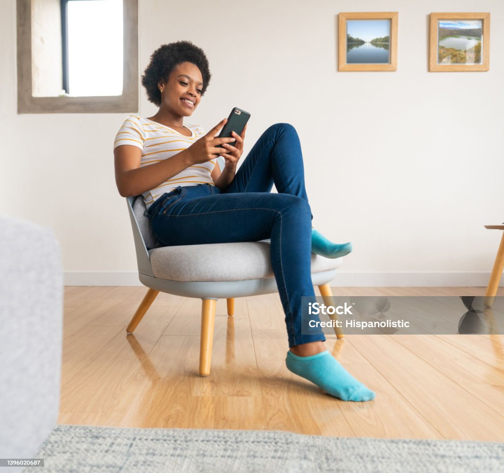 Happy woman relaxing at home and texting on her cell phone Happy African American woman relaxing at home and texting on her cell phone while smiling - lifestyle concepts Women Stock Photo