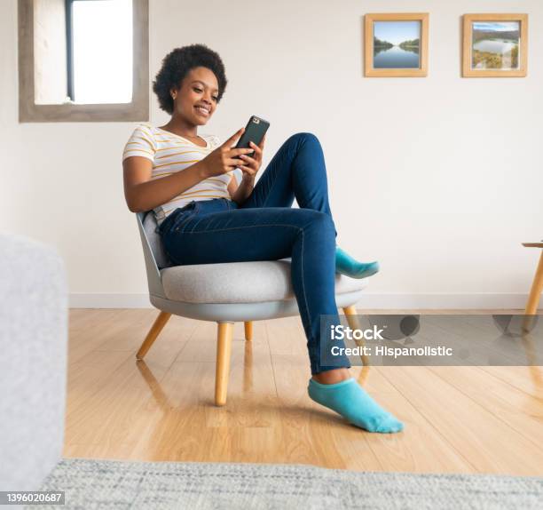 Happy Woman Relaxing At Home And Texting On Her Cell Phone Stock Photo - Download Image Now