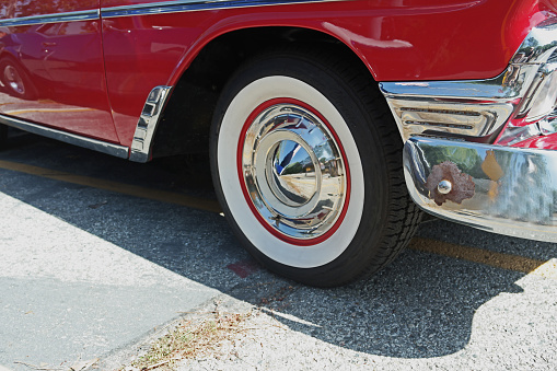 A vintage red car.  Chrome hubcap. Whitewall tires.  Chrome bumper.