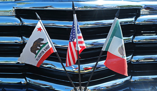 Three flags on a chrome grill.  California flag.  USA Flag.  Mexico flag.