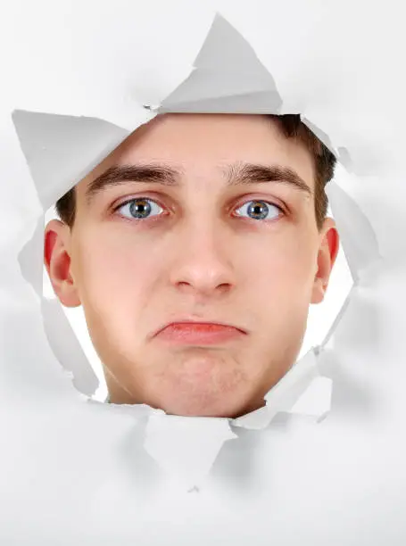 Sad Teenager peeking through Paper Hole