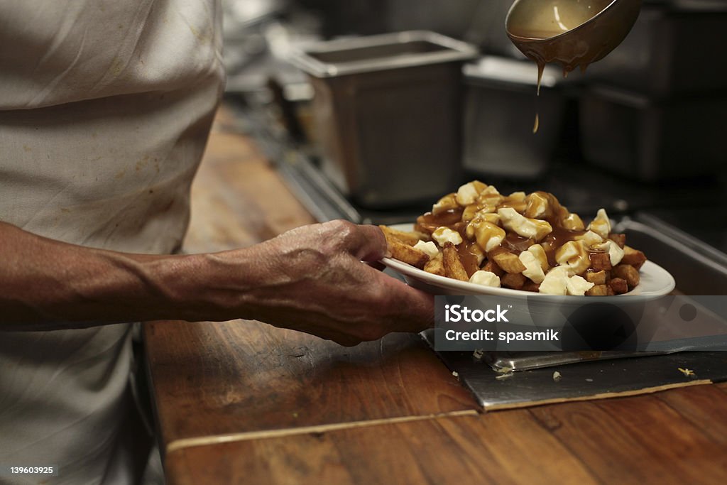 Close-up of chef hands preparing a dish of poutine French fries, cheese curds and gravy, a french canadian traditional plate Poutine Stock Photo