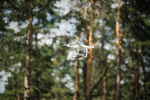 White quadrocopter flies against the background of a green forest