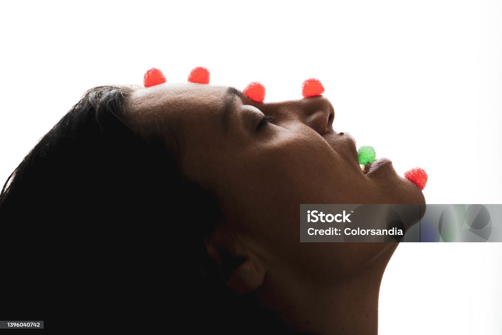 woman with candy gummies on the face. backlit woman eating jelly beans and balancing with jelly beans on her face Candy Stock Photo