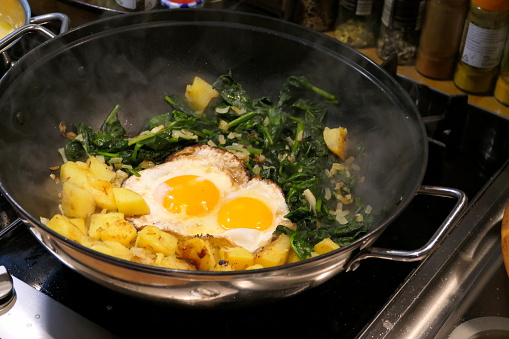 Bavaria, Germany.  Fried eggs, potatoes and spinach on a Gas Stove in a frying pan as part of a simple Bavarian peasant meal.