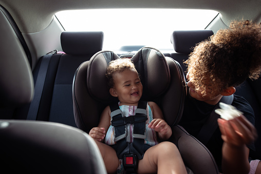 Sisters playing together while driving in the car. The older child pull out pacifier of baby. Traveling with friends, having fun and safe trip, sitting in back seat.