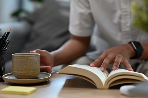 Close up men hands touching the book and holding a cup, reading a book and having a coffee or a tea, for lifestyle, education and home concept.