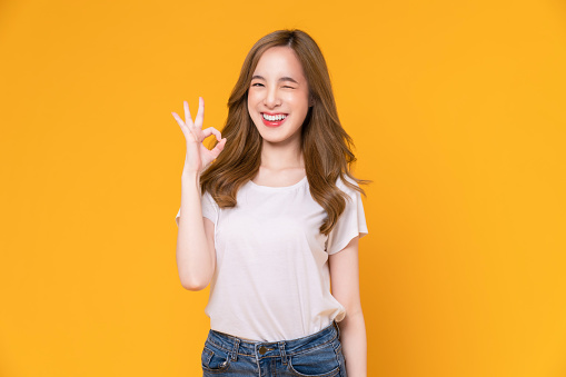 Portrait happy Asian woman shows ok sign and looking at the camera on yellow background.