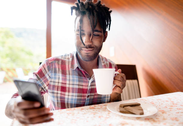 istock Young man sitting at home drinking coffee and checking his phone 1396053029